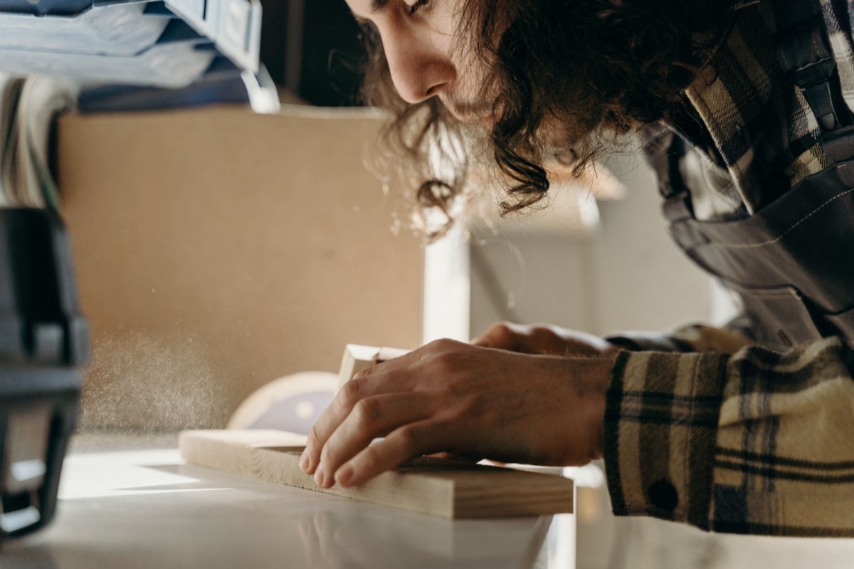 A person sanding the leg of an old wooden chair with sandpaper