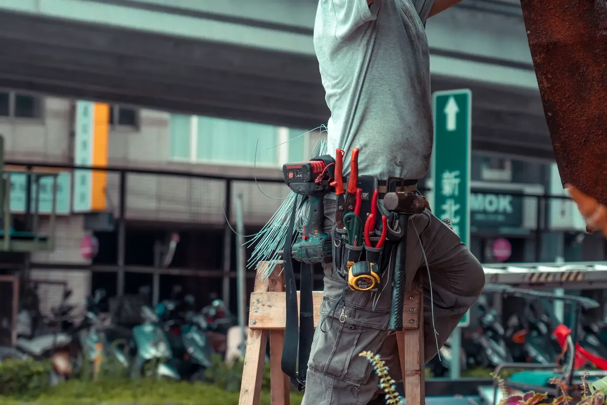 ハンドマンが段ボールに立って工具ベルトを装着し、外に見える工具を持って修理しています。