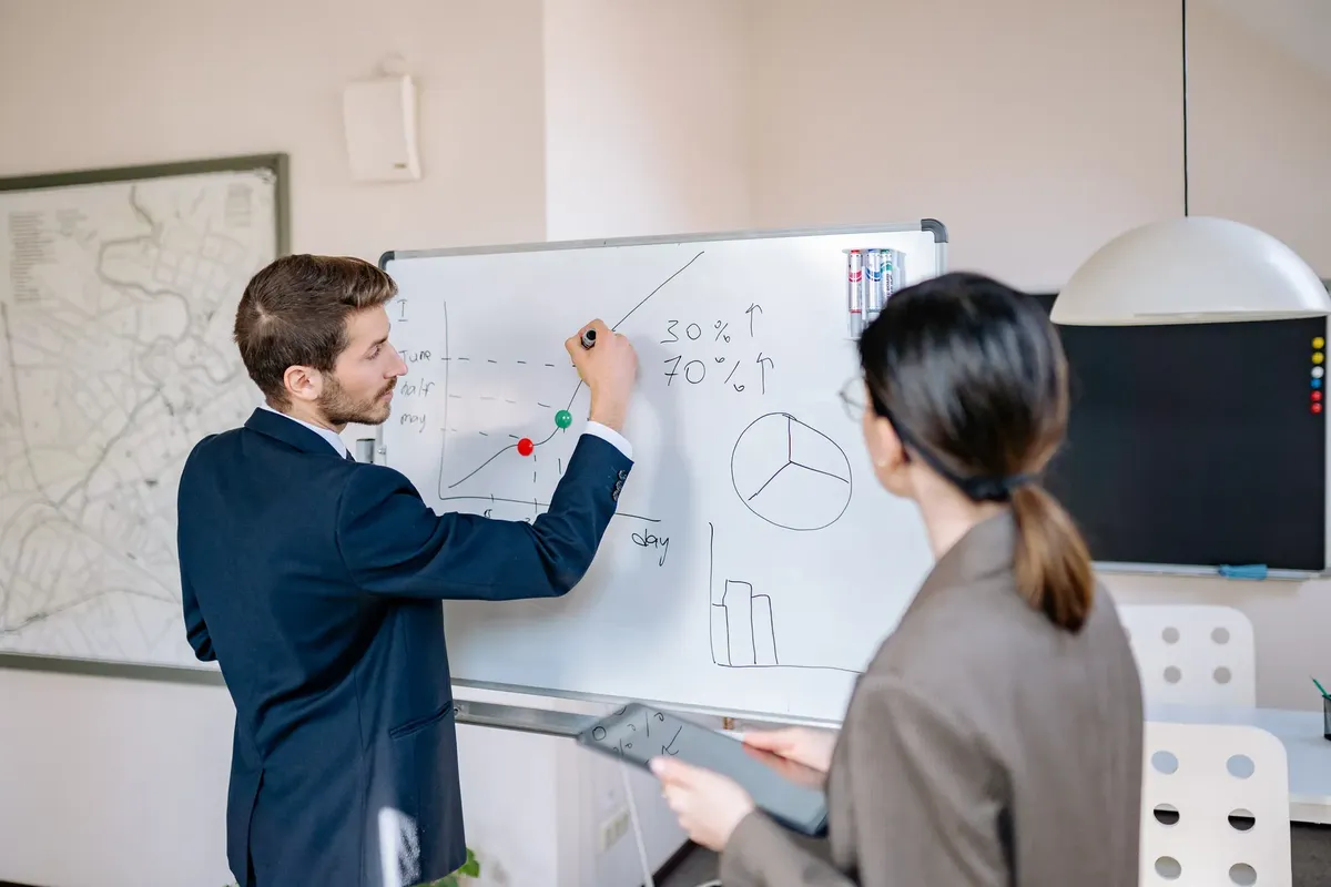 Two business professionals planning and discussing strategy at a whiteboard in a modern office setting.